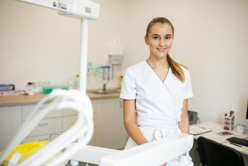 Jauna odontologė su medicinine apranga stovi moderniame odontologijos kabinete prie įrangos